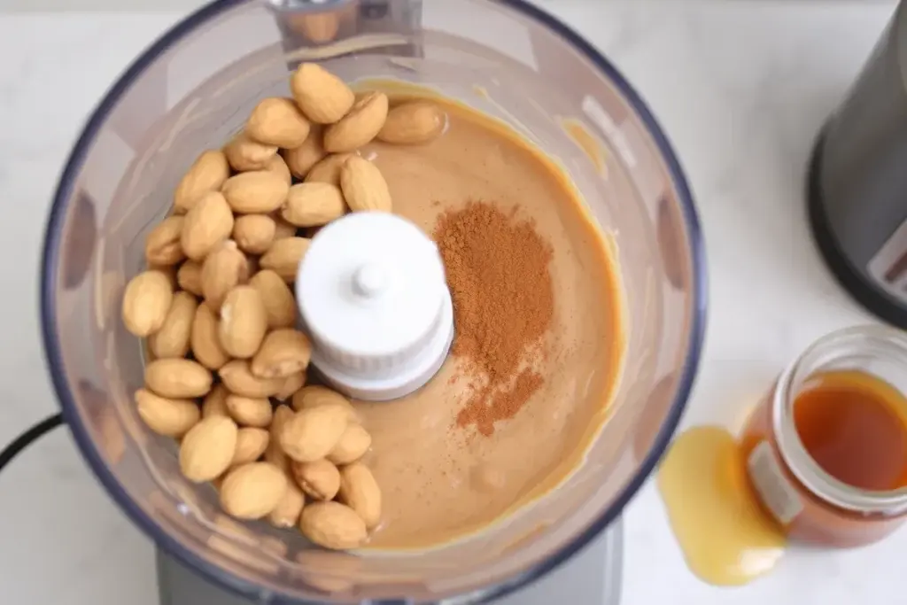 Roasted peanuts and cinnamon blending into peanut butter in a food processor.