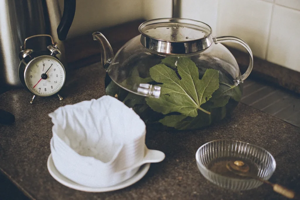 Fresh fig leaves being steeped in a clear teapot for tea preparation.